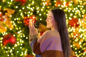 Asian beautiful woman in a colorful sweater stands happily. In his hand he held a light in front of the Christmas tree. With bokeh as background In the theme of Christmas and New Year celebrations
